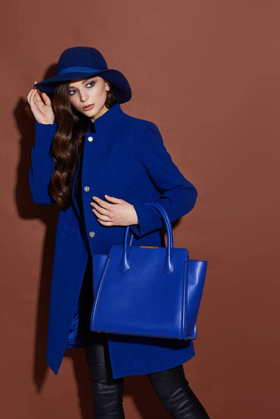 High fashion portrait of young elegant woman. Blue coat, hat, bag. Brown background - Fotó, kép