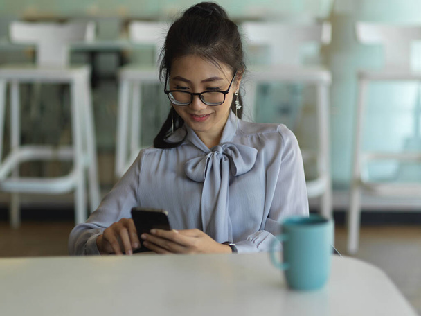 Portret van een zakenvrouw met behulp van smartphone, terwijl een pauze met koffie op de werktafel - Foto, afbeelding