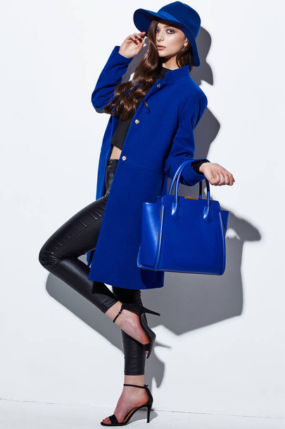 High fashion portrait of young elegant woman. Blue coat, hat, bag. White background - Фото, изображение