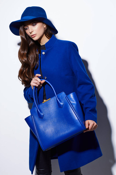 High fashion portrait of young elegant woman. Blue coat, hat, bag. White background - Fotó, kép