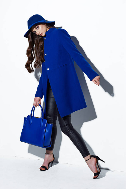 High fashion portrait of young elegant woman. Blue coat, hat, bag. White background - Fotó, kép
