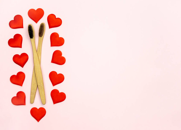 Flat lay composition with hearts shape with bamboo toothbrushes and space for text on pink background, top view. Ecology concept with healthy lifestyle. - Foto, afbeelding