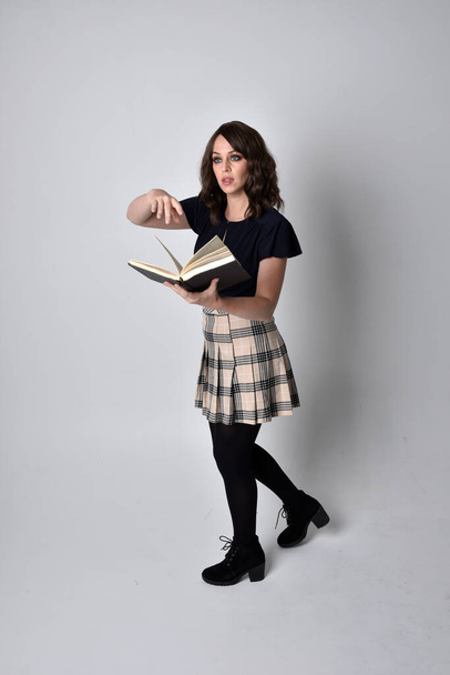 portrét krásné brunetky v kostkované sukni a botách. Stojící póza držení knih na pozadí studia. - Fotografie, Obrázek