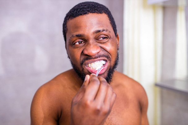 afrikai férfi fogkefe a fürdőszobában nézi tükör - Fotó, kép