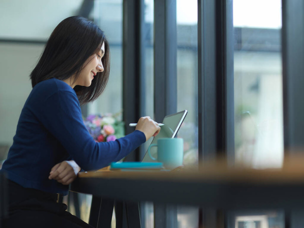 Πλευρική άποψη της φοιτήτρια κάνει ανάθεση με tablet σε ξύλινο μπαρ στο καφέ - Φωτογραφία, εικόνα