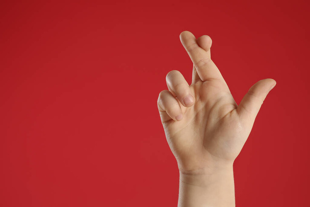 Child holding fingers crossed on red background, closeup with space for text. Good luck superstition - Fotó, kép