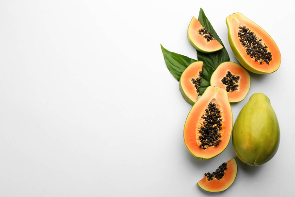 Fresh ripe papaya fruits with green leaves on white background, flat lay. Space for text - Foto, afbeelding