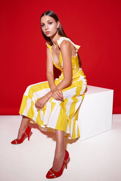 Fashion portrait of young elegant woman. Yellow dress with white strips. Red background - Photo, image