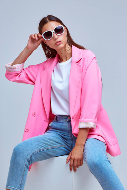 fashion portrait of young elegant woman. Pink jacket, blue jeans, sunglasses. Studio shot - Foto, immagini