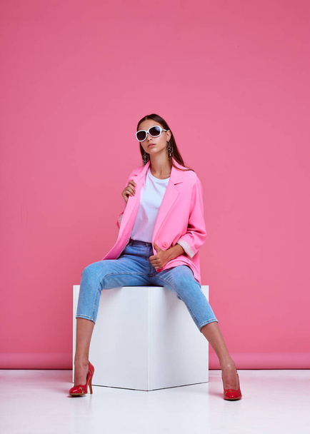 fashion portrait of young elegant woman. Pink jacket, blue jeans, sunglasses. Studio shot - Fotó, kép