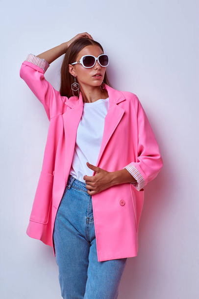 fashion portrait of young elegant woman. Pink jacket, blue jeans, sunglasses. Studio shot - Fotoğraf, Görsel