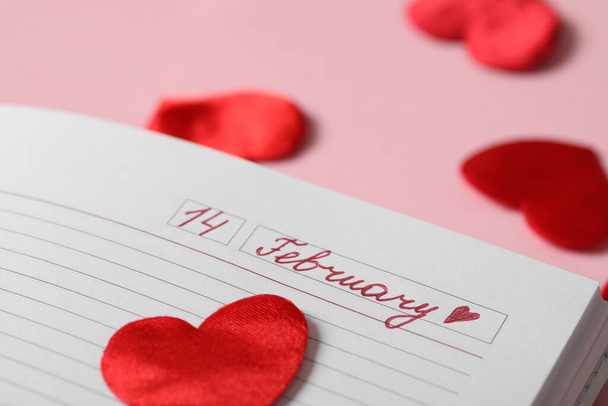 Notebook with 14 February written on page corner against pink background, closeup. Valentine's Day celebration - 写真・画像