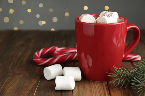 Hot drink with marshmallows in red cup, fir branch and candy canes on wooden table - Foto, Bild