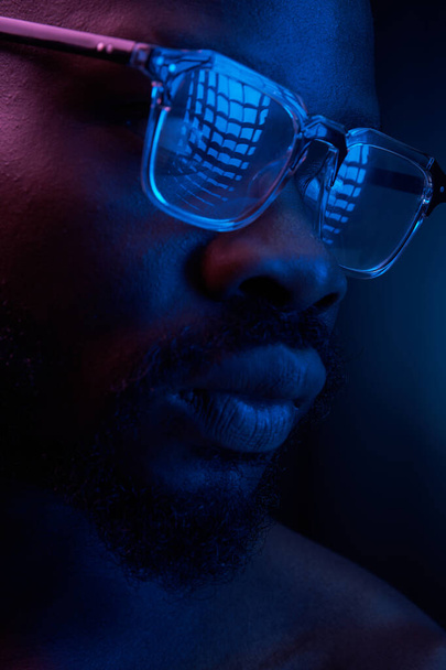 portrait of a handsome black man in red and blue light on dark background  with glasses on his eyes, he has naked sports torso  - Zdjęcie, obraz