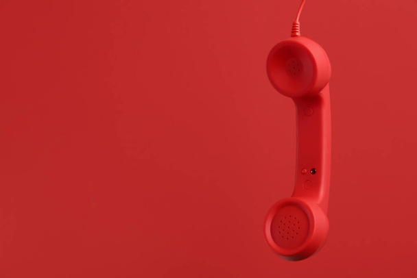Corded telephone handset hanging on red background, space for text. Hotline concept - Fotografie, Obrázek