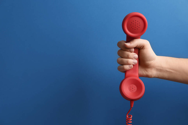Closeup view of woman holding red corded telephone handset on blue background, space for text. Hotline concept - Photo, Image