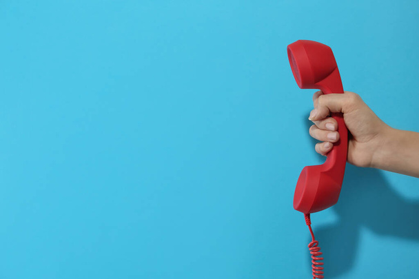 Closeup view of woman holding red corded telephone handset on light blue background, space for text. Hotline concept - Photo, Image