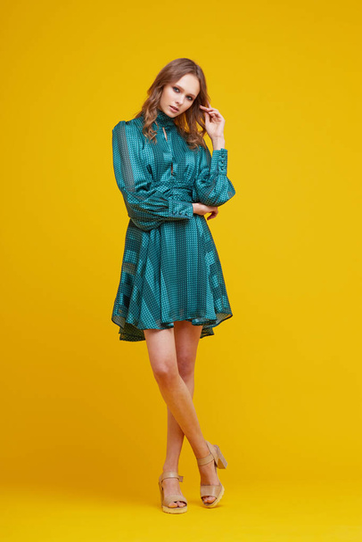 Beautiful young woman in green dress. Yellow background, fashion studio shot. - Foto, Imagem