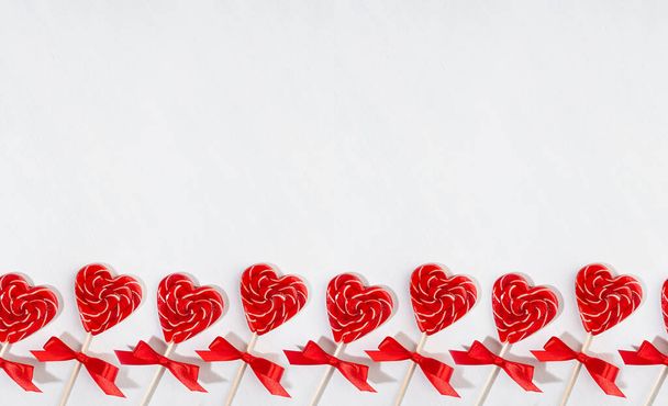 Bright valentine's day background - sweet red lollipops hearts on white wood board as seamless border, layout for banner, header, design. - Foto, Imagen