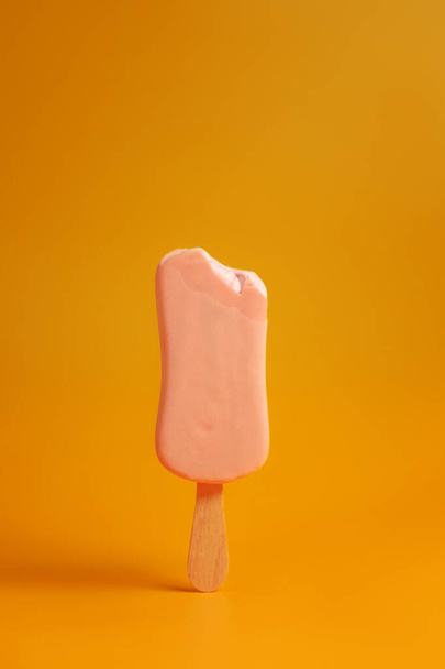 pink ice cream popsicle on yellow background bitten off a piece - Foto, immagini