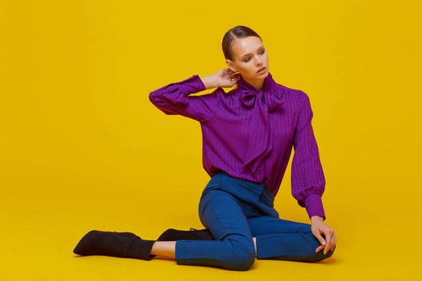 High fashion portrait of young elegant woman. Sudio shot. Violet blouse, blue pants, ankle boots, yellow background - 写真・画像