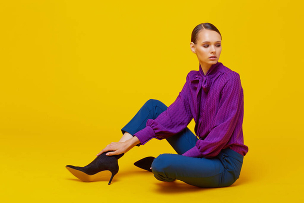 High fashion portrait of young elegant woman. Sudio shot. Violet blouse, blue pants, ankle boots, yellow background - Foto, immagini