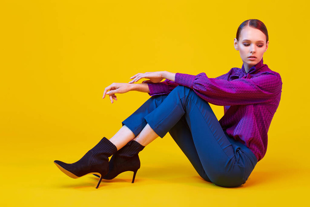 High fashion portrait of young elegant woman. Sudio shot. Violet blouse, blue pants, ankle boots, yellow background - Фото, зображення