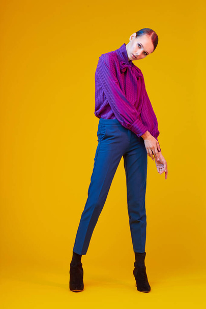 High fashion portrait of young elegant woman. Sudio shot. Violet blouse, blue pants, ankle boots, yellow background - Foto, Imagen
