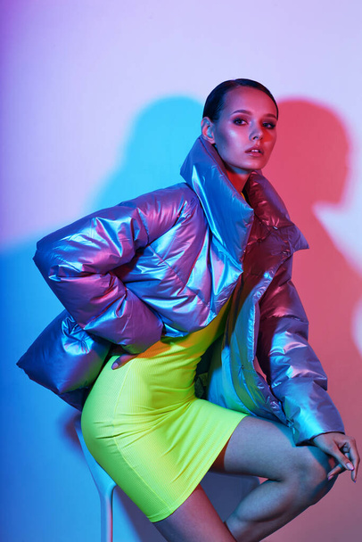 Fashion portrait of young elegant woman. Silver down jacket, neon light - Фото, зображення