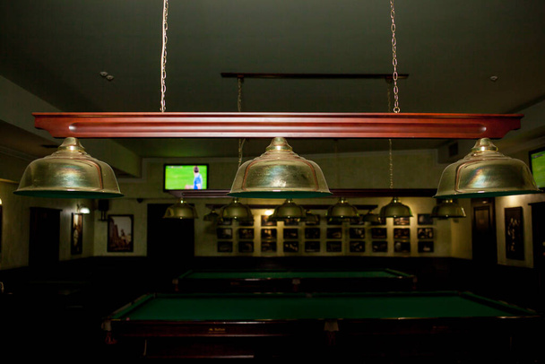 Лампы в бильярдном клубе. Лампы над бильярдным столом светят в темноте. Зеленые бильярдные столы и лампы. Интерьер бильярдного зала - Фото, изображение