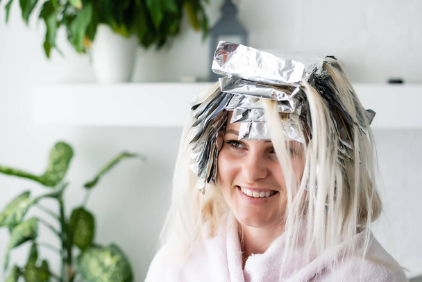 Bella giovane donna con un foglio di alluminio sui capelli. Processo di sbiancamento o tintura a casa - Foto, immagini