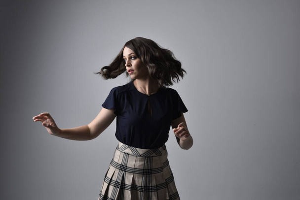 Close up portrait of pretty brunette woman wearing tartan skirt and blouse.  Posing with gestured hands against a  studio background. - Photo, Image