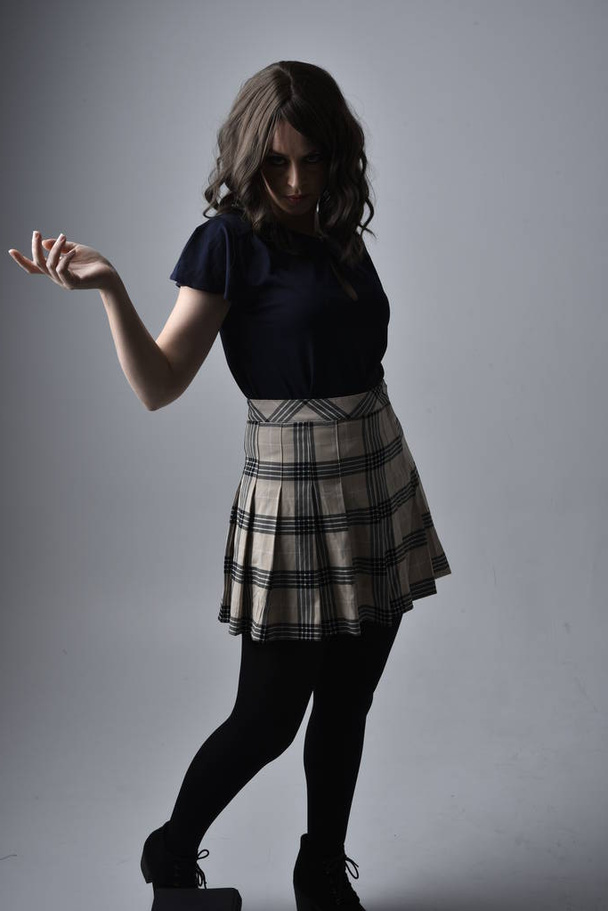 Close up portrait of pretty brunette woman wearing tartan skirt and blouse.  Posing with gestured hands against a  studio background. - Фото, изображение