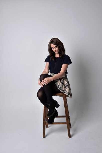 Nahaufnahme Porträt einer hübschen brünetten Frau mit Schottenrock und Bluse. Sitzpositionen vor Studiohintergrund. - Foto, Bild