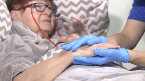 Verzorger die de hand van de patiënt vasthoudt, thuiszorg, hulp bij het verpleeghuis. Oudere vrouw in bed met een verpleegster thuis. Handjes bij elkaar houden. - Video