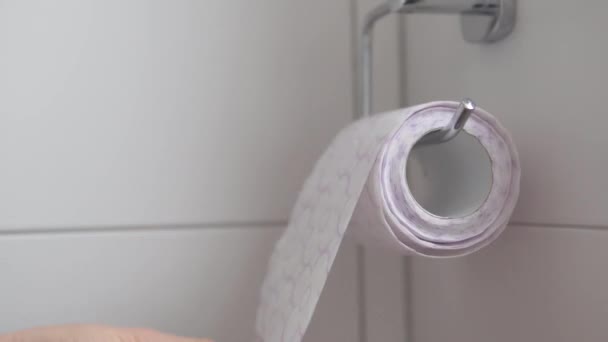 Ένα γυναικείο χέρι κόβει ένα κομμάτι χαρτί τουαλέτας από ένα ρολό που κρέμεται στο δωμάτιο της τουαλέτας - Πλάνα, βίντεο