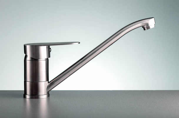 Close up of modern kitchen faucet on dark color countertop. - Foto, afbeelding