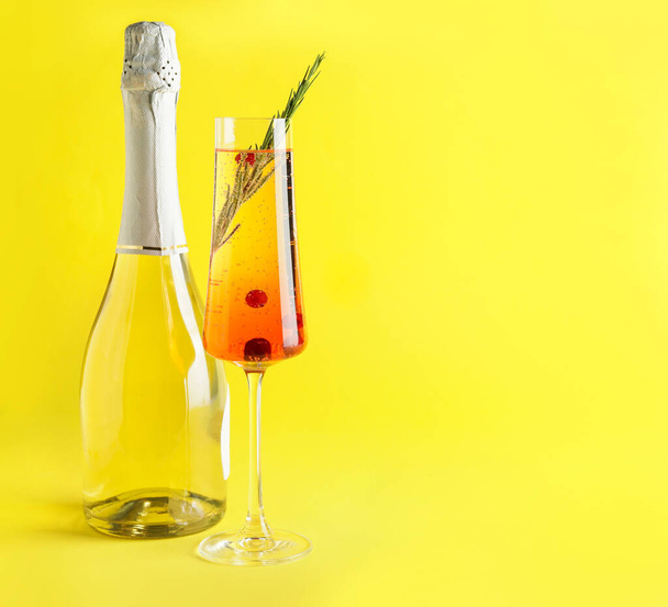 Bottle of champagne and cocktail with cranberry and rosemary in glass on color background - Фото, зображення