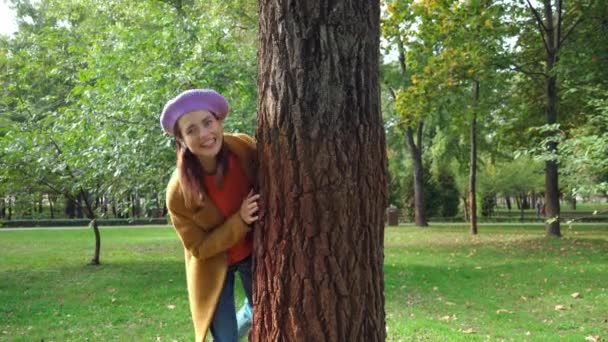 mujer alegre escondida detrás del tronco del árbol en el parque - Metraje, vídeo