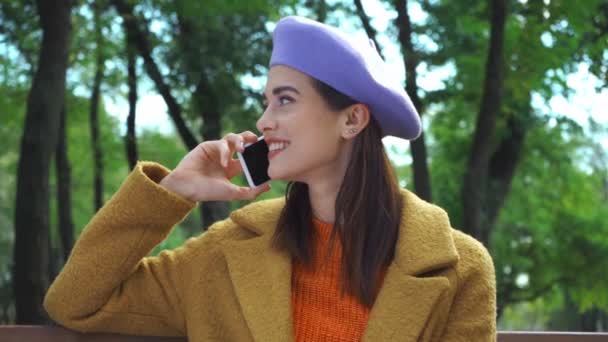 donna eccitata che parla sul cellulare mentre è seduto nel parco autunnale - Filmati, video
