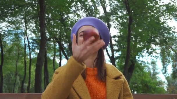 wesoła kobieta żongluje dojrzałym jabłkiem i pokazuje go przed kamerą w parku - Materiał filmowy, wideo