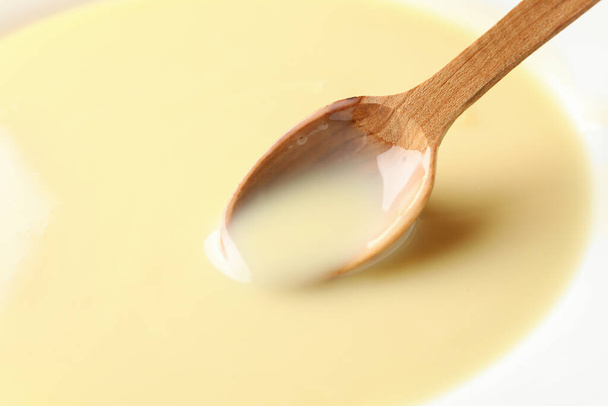 Wooden spoon in condensed milk, close up - Zdjęcie, obraz