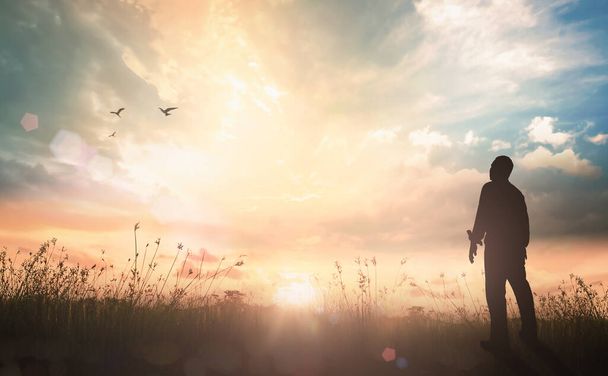 Palvonta ja ylistys käsite: Siluetti nöyrä mies seisoo auringonvalossa niitty syksyllä auringonlaskun taustalla - Valokuva, kuva