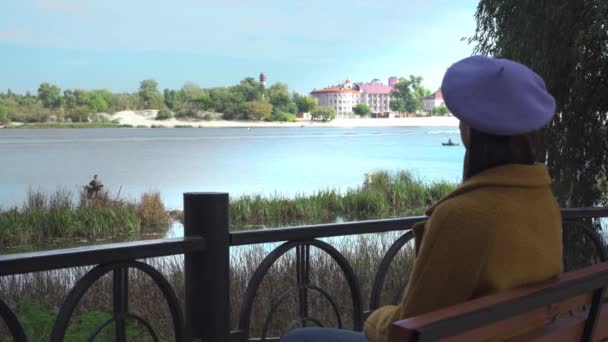 jonge vrouw zitten op de brug in het park en kijken naar de rivier - Video
