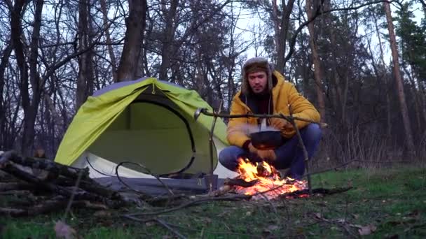 Un uomo vicino a un falò e una tenda nella foresta - Filmati, video