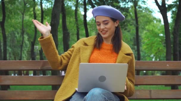 szczęśliwy freelancer jesienią strój macha ręką podczas rozmowy wideo w parku - Materiał filmowy, wideo