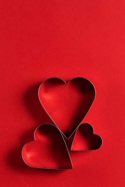 Saint Valentine day minimalistic greeting card, heart-shaped cookie cutters on red background with beautiful shadows, flat lay - Photo, image