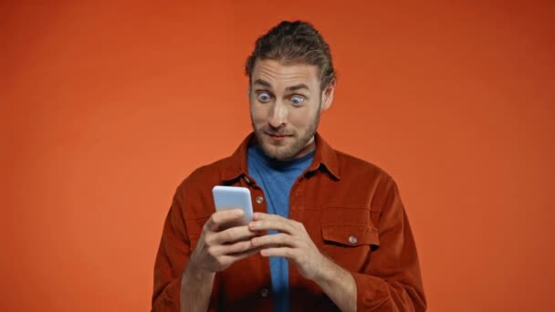 ενθουσιασμένος άνθρωπος τζόγου στο smartphone και δείχνει χειρονομία νίκη απομονώνονται σε πορτοκαλί - Πλάνα, βίντεο