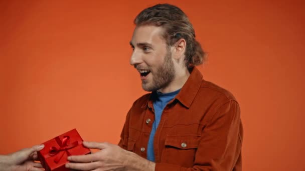 hombre complacido tomando regalo de San Valentín de mujer aislada en naranja - Imágenes, Vídeo