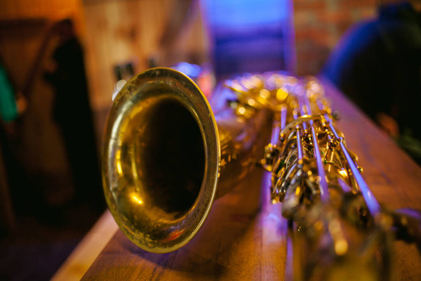 Zblízka fotografie lesklého zlatého saxofonu. Vintage Saxophone. Zlatý soprán Saxofon. Větrný hudební nástroj. Krásný zlatý saxofon na dřevěném pozadí - Fotografie, Obrázek